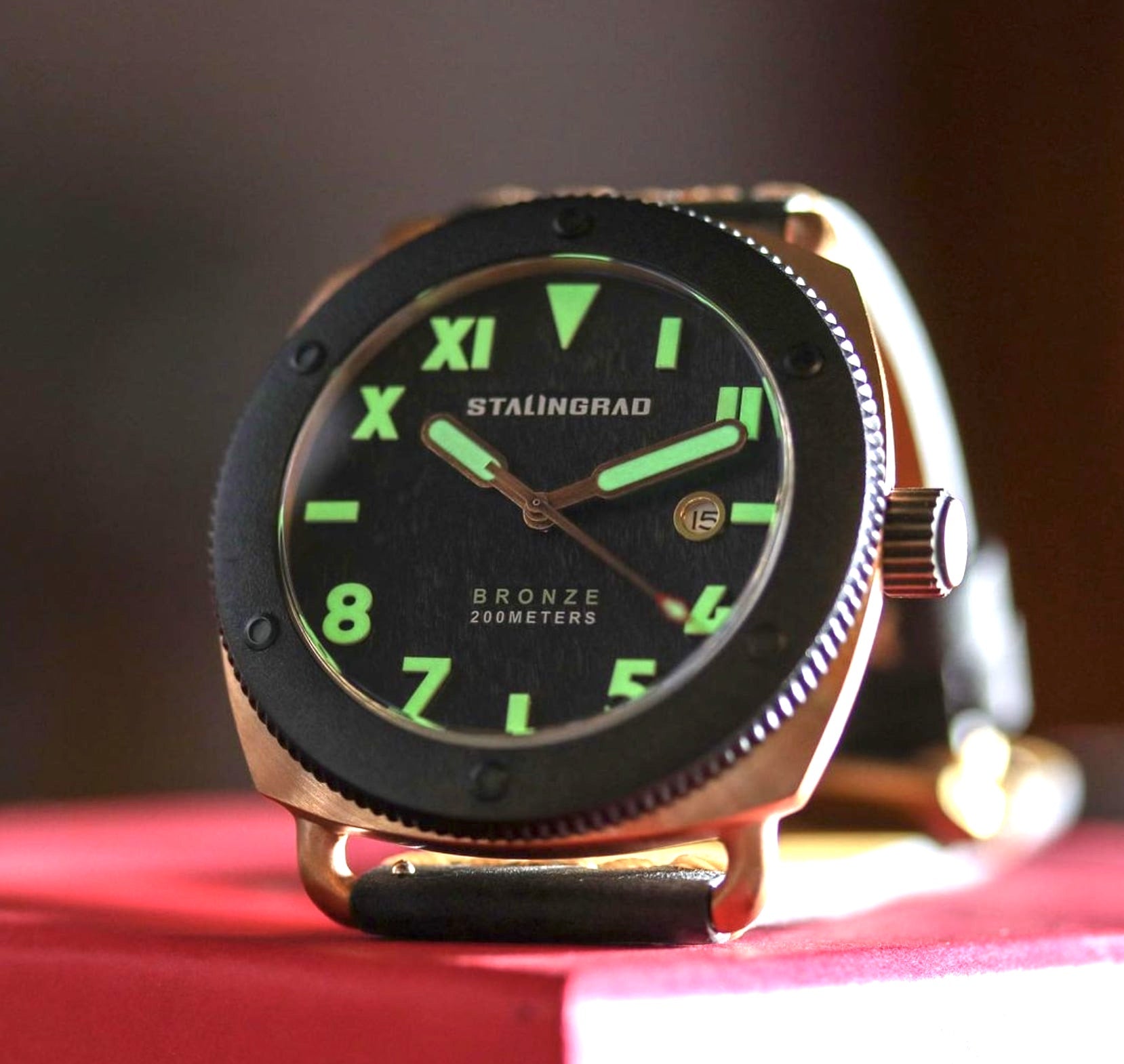 Stalingrad Bronze Defender 200m mens watch on a red table, with lume glowing on the hands and dial