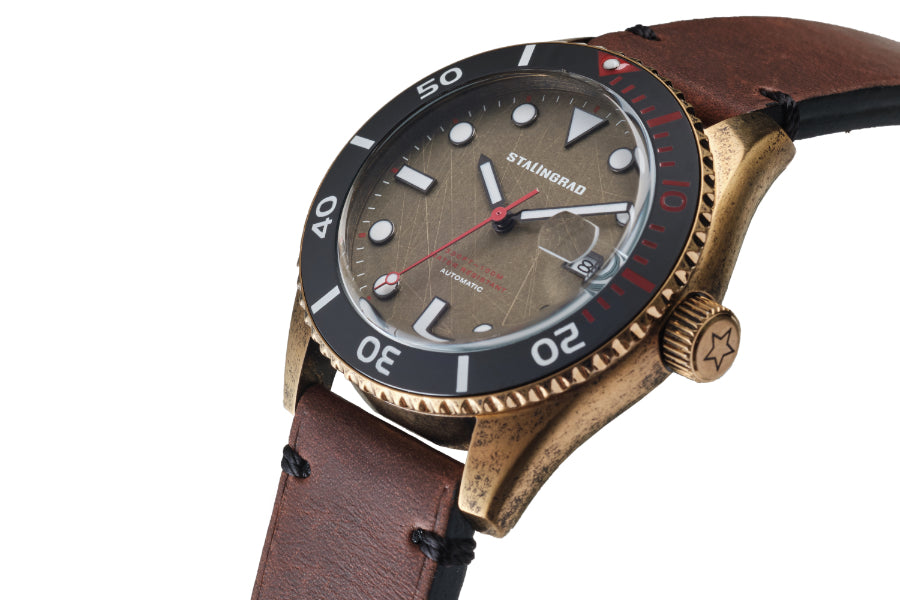 Stalingrad Volga defender automatic watch with a brass case and brass colour dial and black bezel with red second hand in a brown leather strap, diagonal view or watch on a white background
