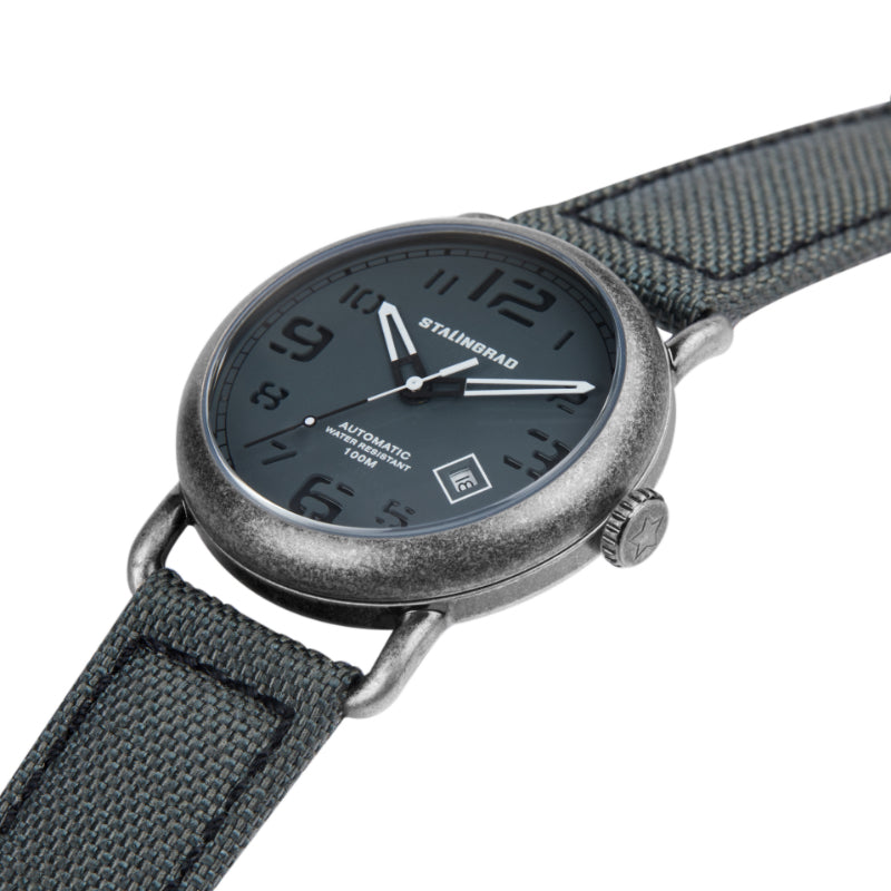 Stalingrad Rodim Watch with a sandwich dial. Grey dial with white hands, Silver case and a grey cordura strap with a brown nato strap next to it diagonal view of watch on white background.